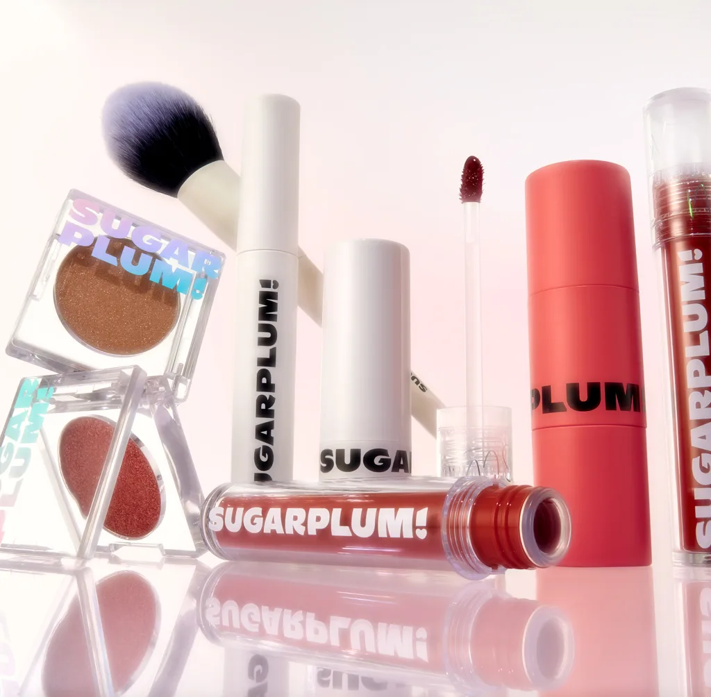 Product flat lay featuring lip gloss tubes and a mobile phone displaying a makeup application close-up for Sugarplum.